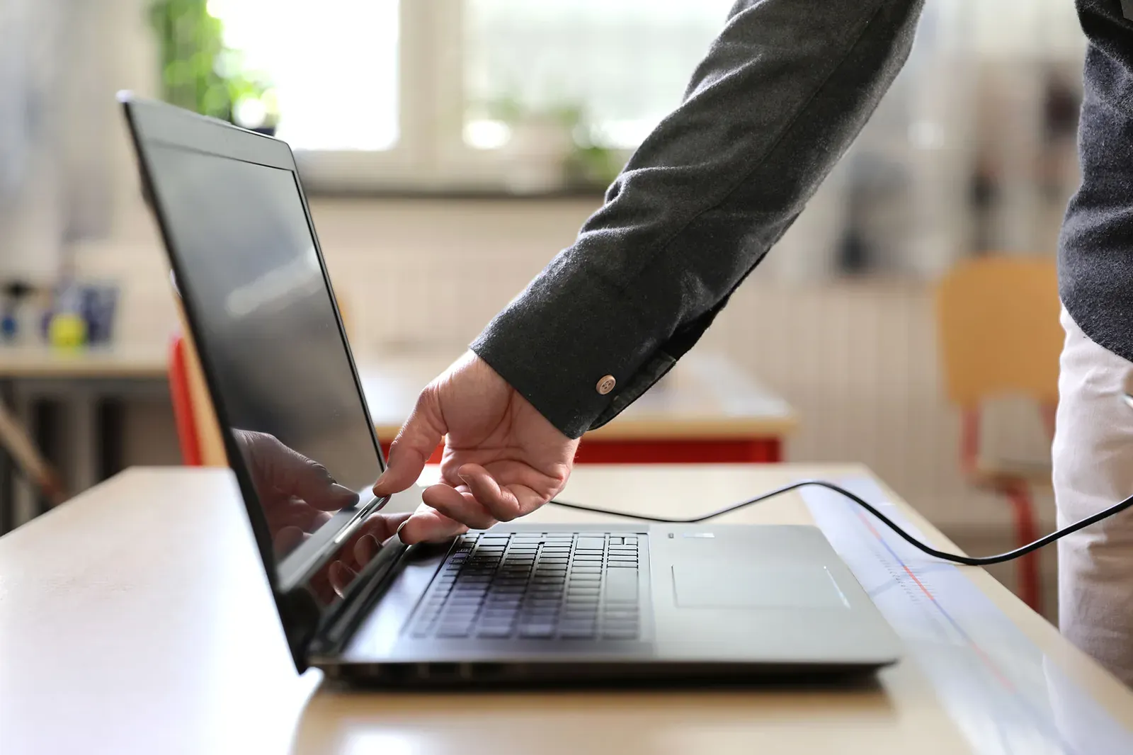 Badacz przygotowuje laptop na ławce w szkolnej klasie; do komputera prowadzi kabel eye trackera