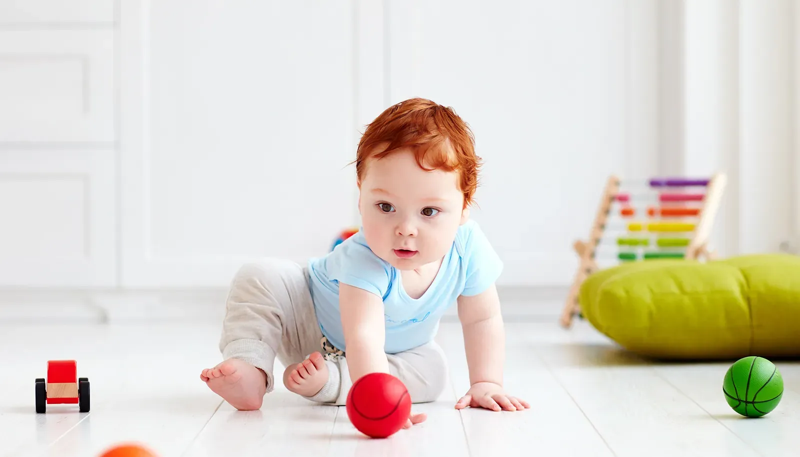 Niemowlę raczkuje po jasnej podłodze wśród zabawek
