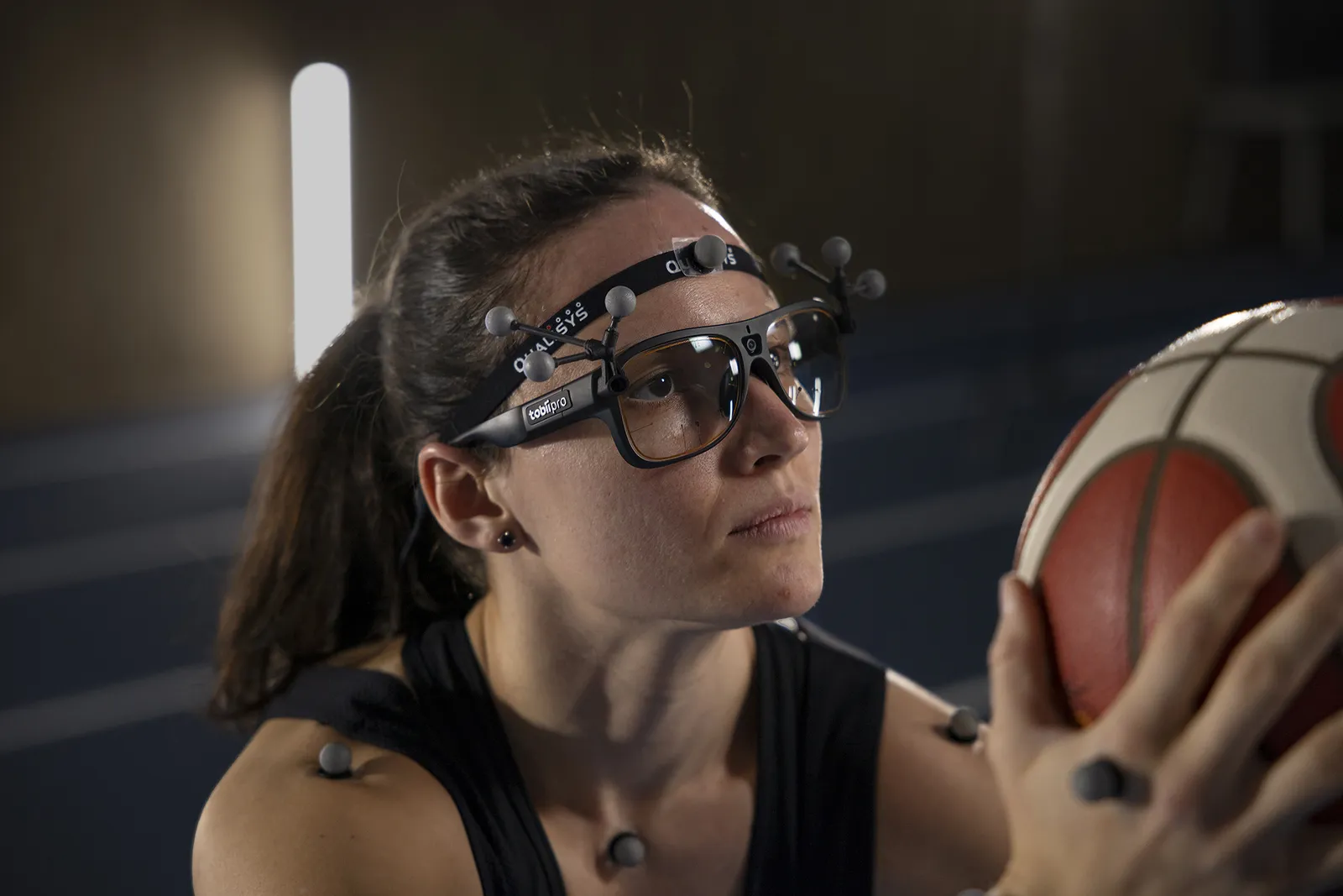 Koszykarka w okularach Tobii Pro Glasses 3 z nakładką markerów motion capture Qualisys i markerami na ciele, trzyma piłkę