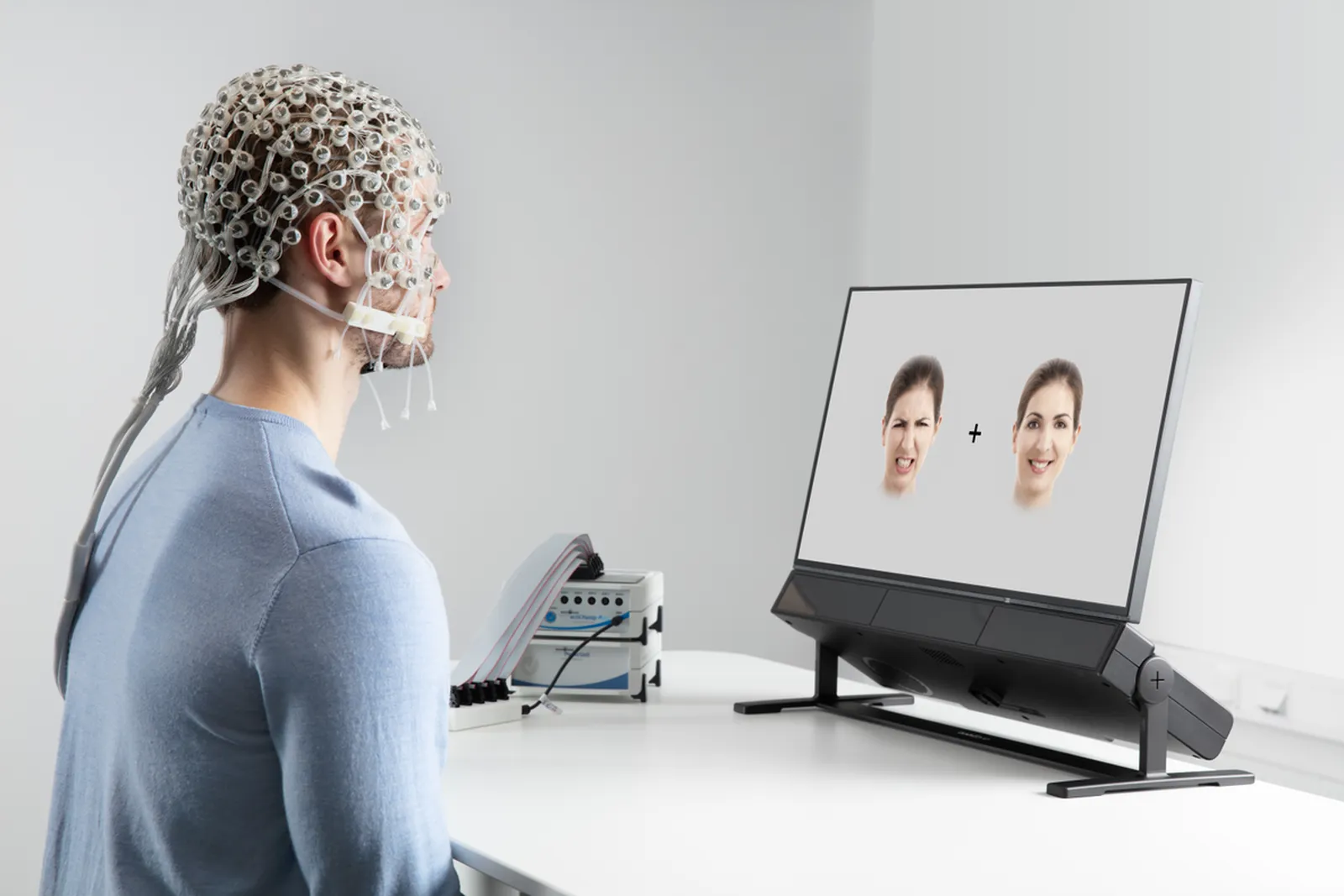 Uczestnik w czepku EEG Brain Products patrzy na zdjęcia twarzy na monitorze z eye trackerem Tobii Pro Spectrum