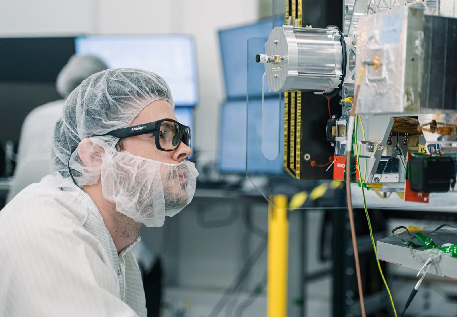 Pracownik w odzieży ochronnej w okularach Tobii Pro Glasses 3 kontroluje urządzenie na hali produkcyjnej