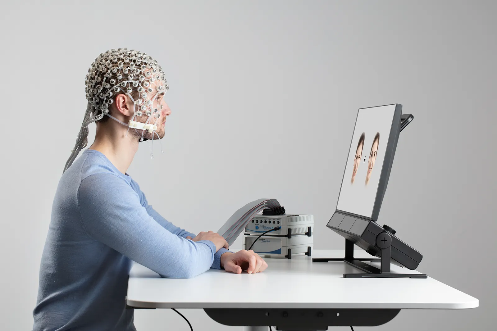 Uczestnik w czepku EEG przed monitorem z Tobii Pro Spectrum; obok wzmacniacz EEG