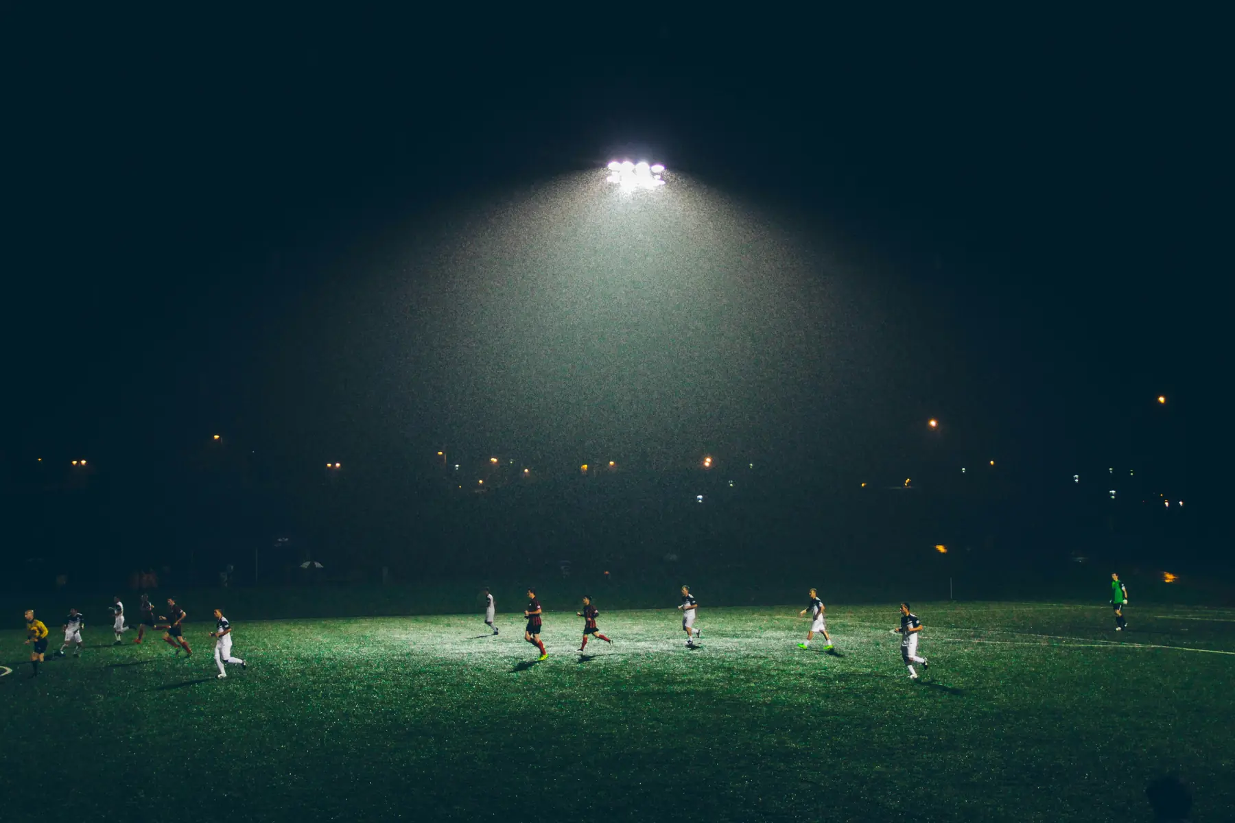 A soccer team on a field at night under a single floodlight