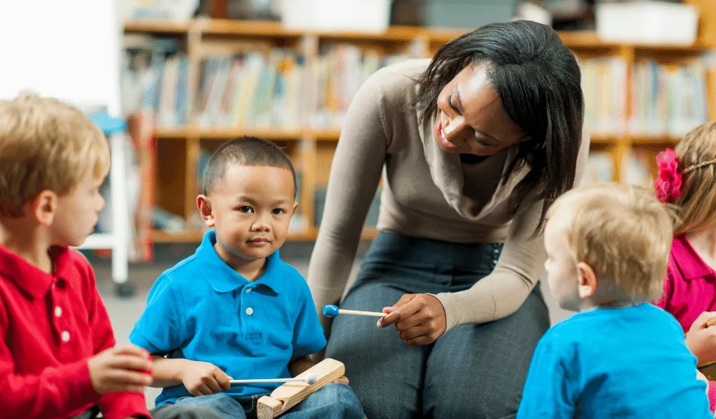 A teacher with a group of young children in a room with books